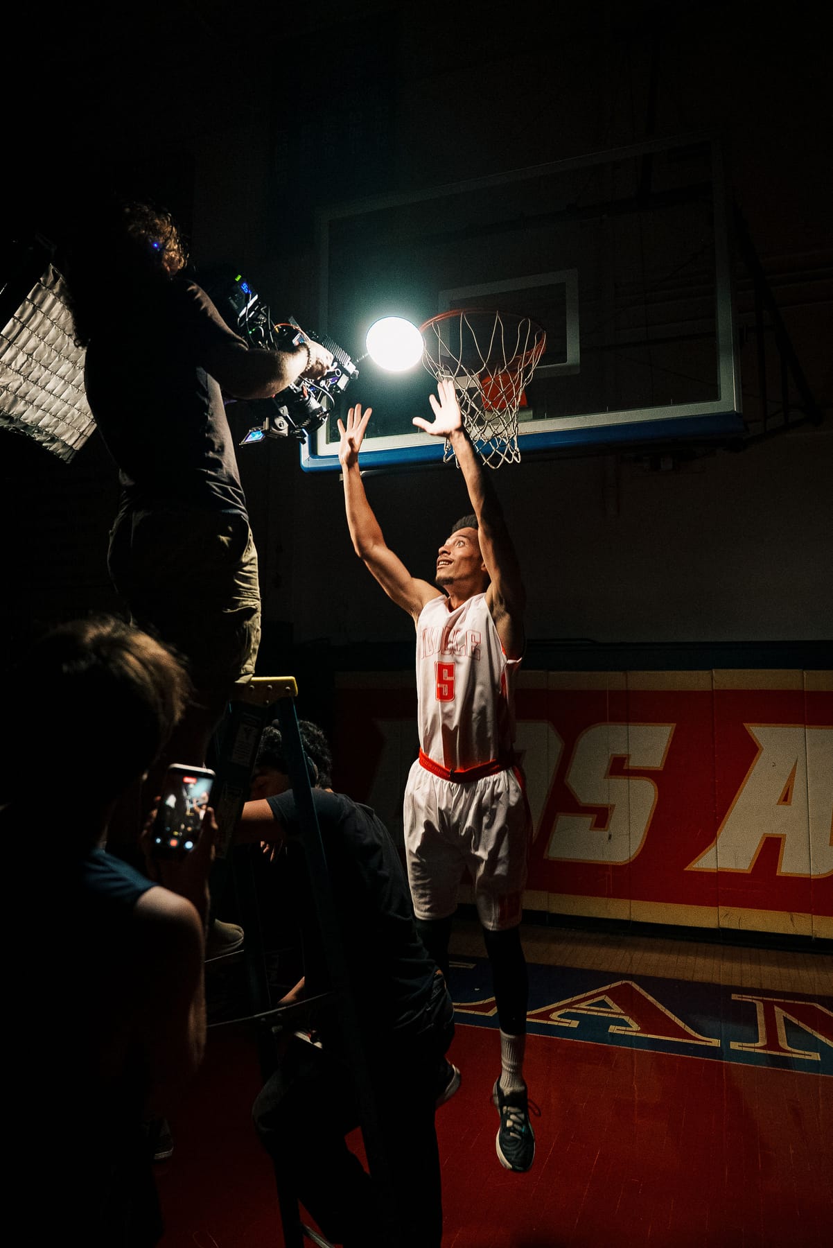 Basketball player reaching for the hoop on a lit set
